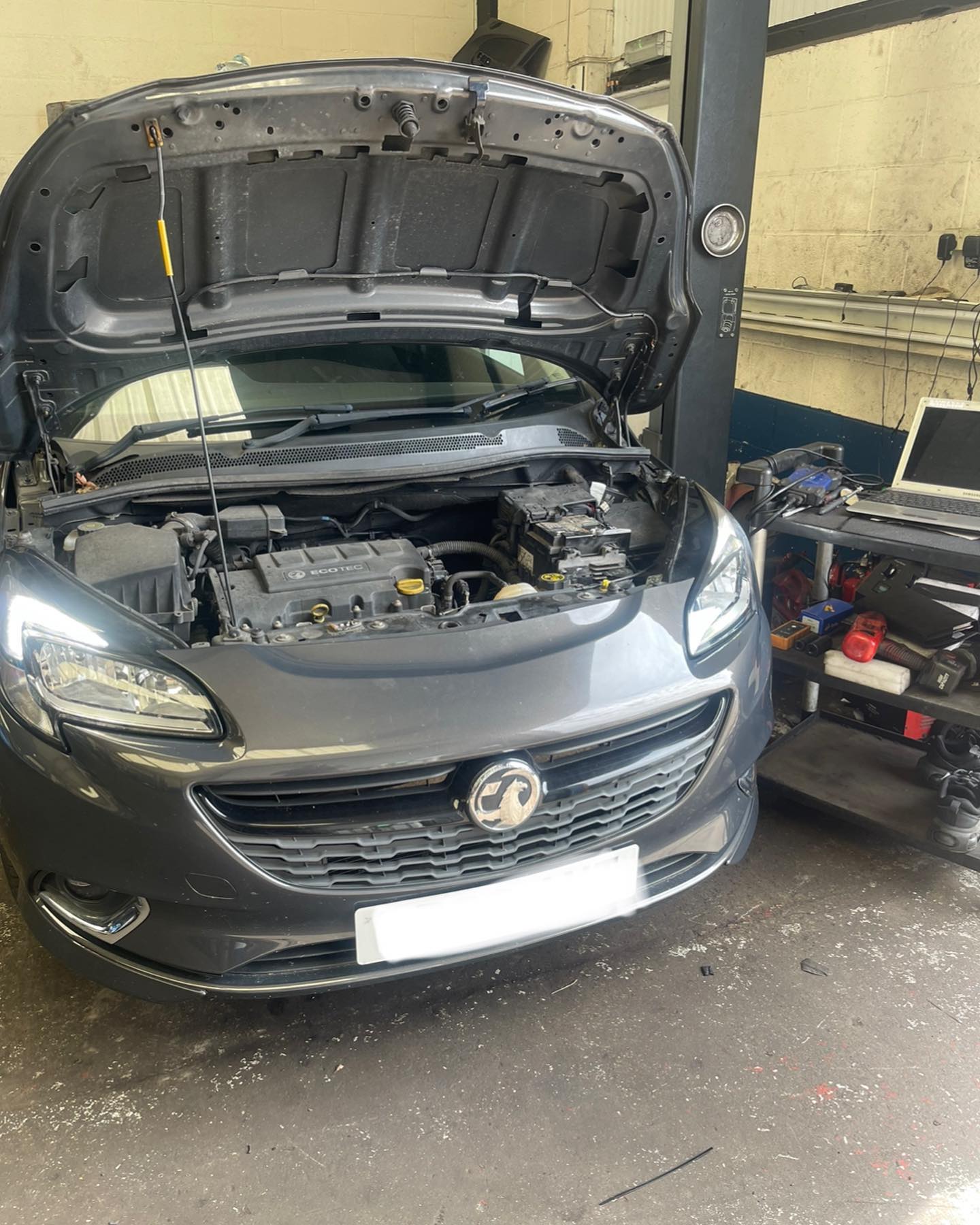 Vauxhall Corsa in the workshop with the bonnet up and a diagnostic laptop on the trolley beside it