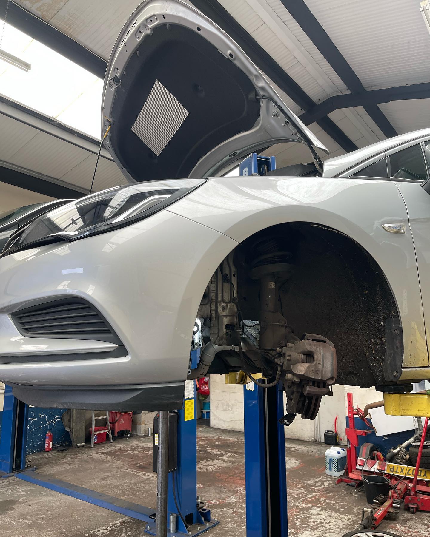 Silver Vauxhall Astra up on a two-post lift with the front wheel off and the suspension exposed